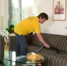 Haushaltshilfe beim Staubsaugen Haushaltshilfe saugt ein Sofa im Wohnzimmer – professionelle Haushaltsreinigung von Home Service Berlin